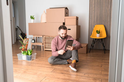 Mature man using his tablet while moving in new unfurnished apartment.