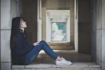 Side view of young woman sitting against wall