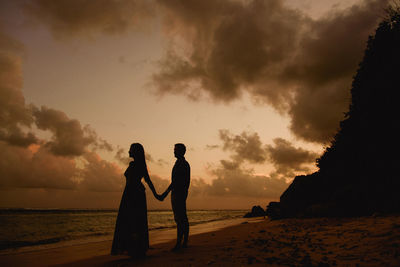Silhouette friends standing on beach against sky during sunset