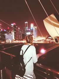 Rear view of woman standing by illuminated bridge against clear sky at night