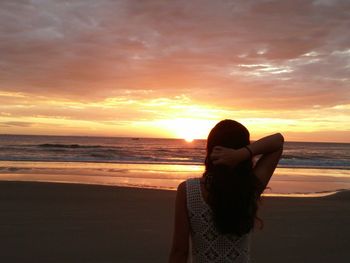 Rear view of woman standing at beach against sky during sunset