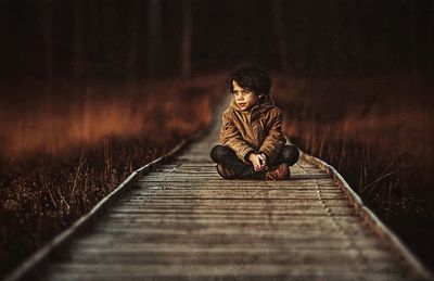 Boy sitting on boardwalk