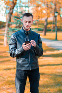 Full length of young man using smart phone while standing on tree