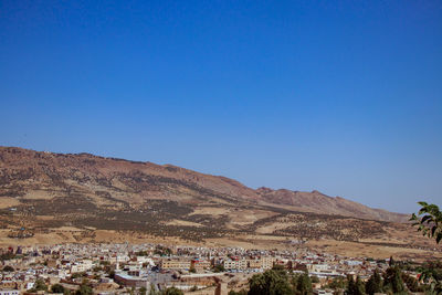 Aerial view of townscape by mountain against clear blue sky