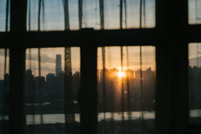 Silhouette buildings against sky during sunset seen through glass window