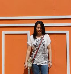 Portrait of woman standing against orange wall