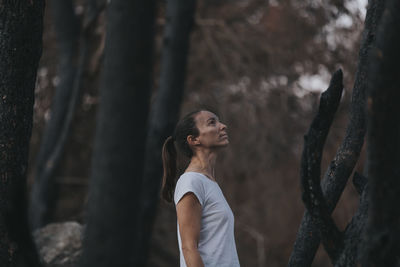 Thoughtful woman standing amidst burnt trees in forest