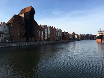 View of buildings by river against sky in city