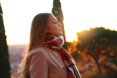 Side view of beautiful woman with eyes closed against sky during sunset