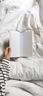 High-key of a hand holding a blank lined notebook in bed with white sheets