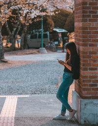 Woman using mobile phone while leaning on brick wall