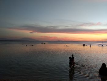 Silhouette people standing on beach against sky during sunset