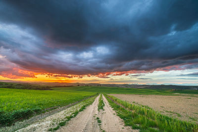 Road amidst field against sky during sunset