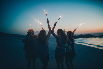 People enjoying at beach against sky during sunset