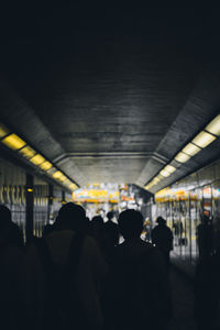 Rear view of people walking on illuminated railroad station platform