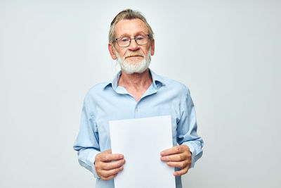 Portrait of senior man holding paper against white background