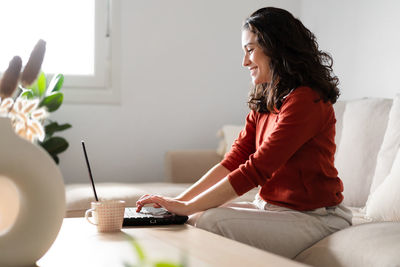 Side view of young woman sitting on sofa at home