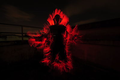 Illuminated red light painting against sky at night