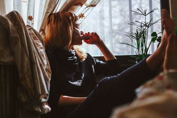 REAR VIEW OF WOMAN SITTING AT WINDOW