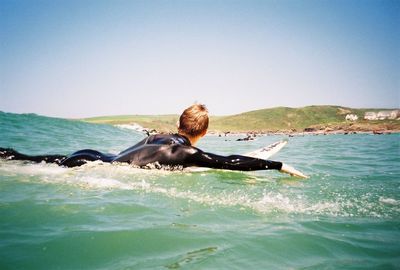 Side view of man surfboarding in sea against sky