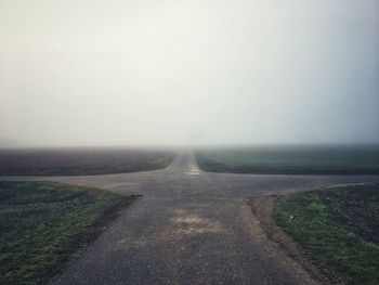 Road amidst field against sky during foggy weather