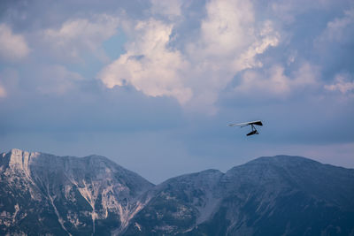 Low angle view of airplane flying in mountains against sky