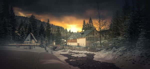 Snow covered houses and trees against sky during sunset