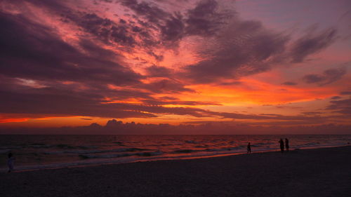 Silhouette people on beach against sky during sunset