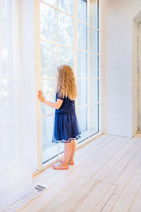 Cute girl in casual clothes standing near the window and watching out