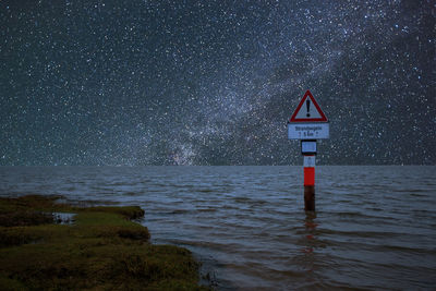 Road sign in sea against sky at night