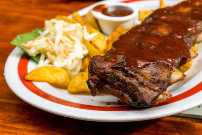 Close-up of grilled meat with french fries in plate on table