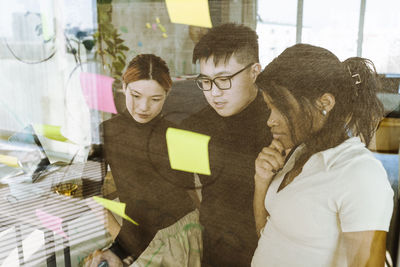 Multiracial male and female colleagues brainstorming over adhesive notes in creative office