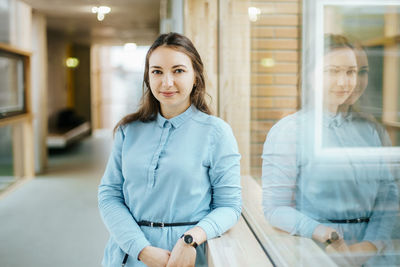 Portrait of happy young businesswoman standing at office corridor