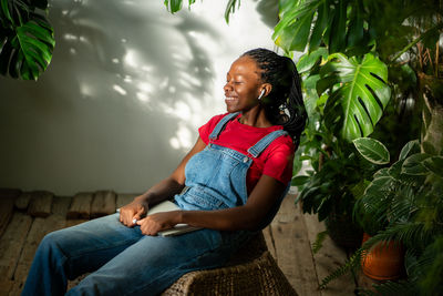 Side view of young woman sitting against plants