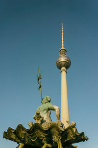 Low angle view of statues and fernsehturm against clear blue sky