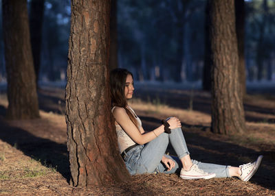 Side view of woman sitting on tree trunk