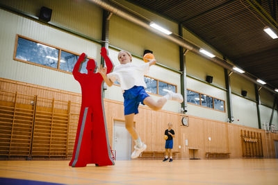Female handball player jumping while throwing handball in sports court