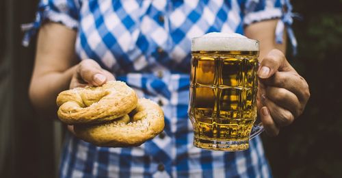 Midsection of woman holding beer glass with croissants