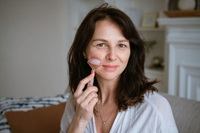 Portrait of caucasian woman doing facial massage with quartz scraper for pink