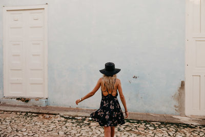 Rear view of woman in hat walking against house