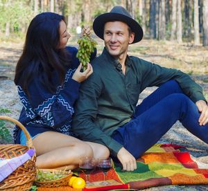 Woman feeding grapes to boyfriend while having picnic in forest