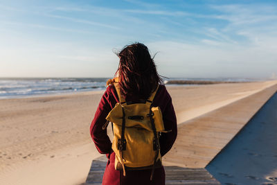 Rear view of woman standing at beach against sky