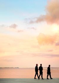 Silhouette people on beach against sky during sunset