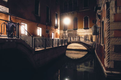 Arch bridge over canal amidst buildings in city at night