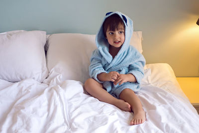 Baby boy two years old in a blue terry robe with a hood lying on a big bed