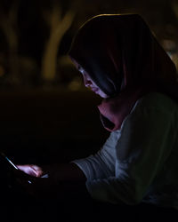 Side view of woman using smart phone while sitting outdoors at night