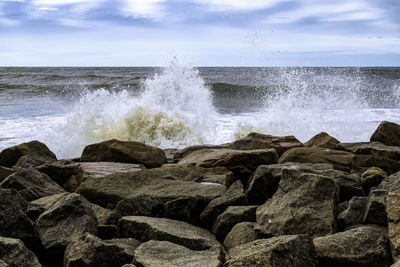 Waves splashing on rocks at shore against sky