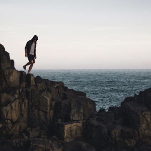 Man standing on cliff by sea against sky
