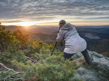 Hiker and photo enthusiast stay with tripod on cliff. peak with woman taking photos in sunrise