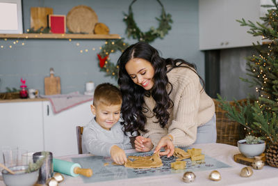 A happy beautiful mother with a young son is cutting out christmas cookie molds from the dough 